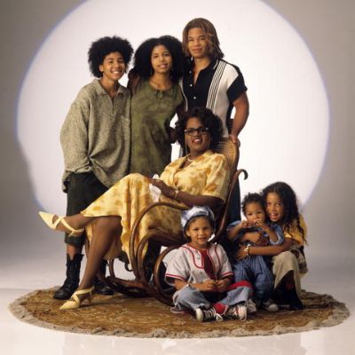 The woman is sitting on a chair while the others surround her.